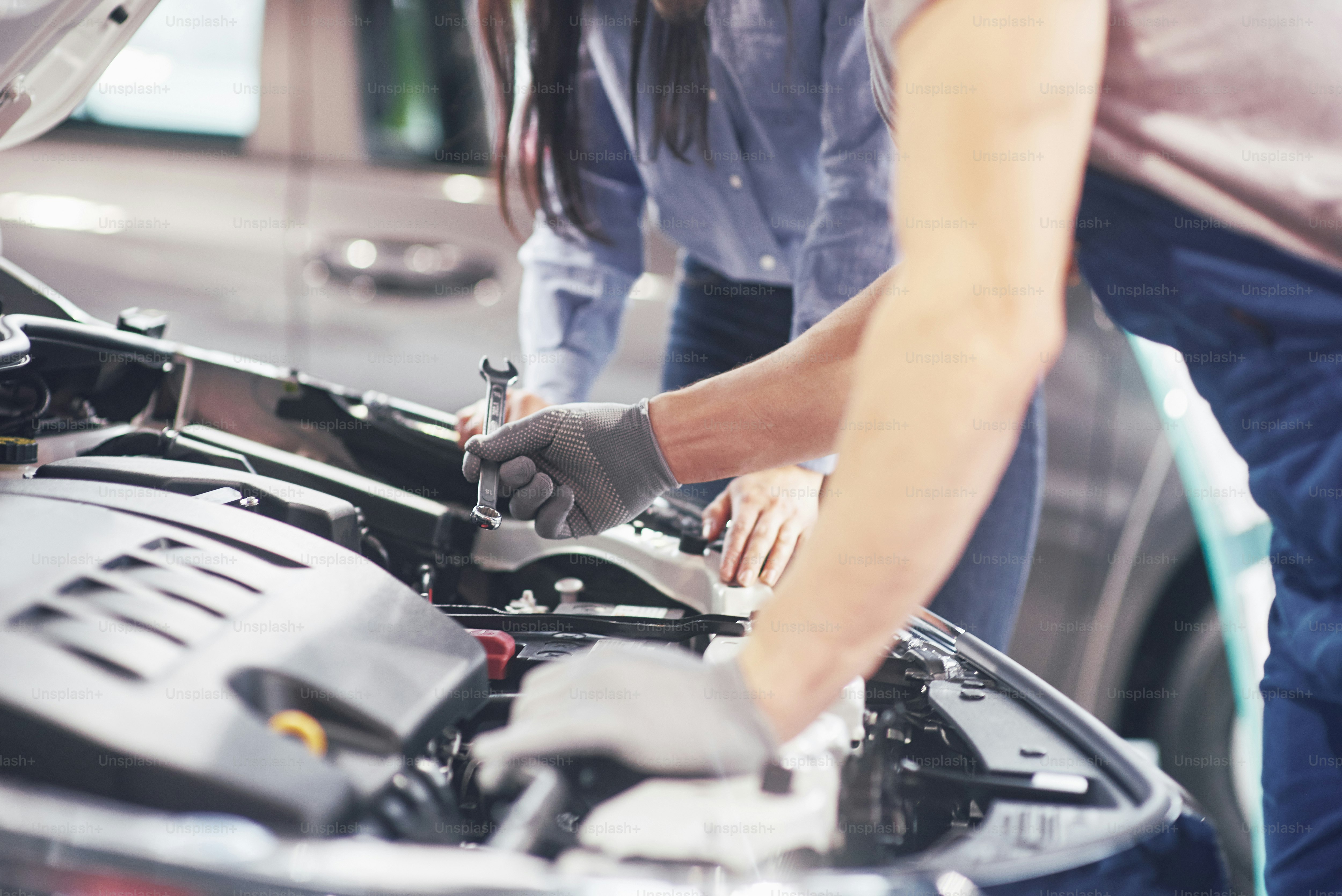 A man mechanic and woman customer look at the car hood and discuss repairs.