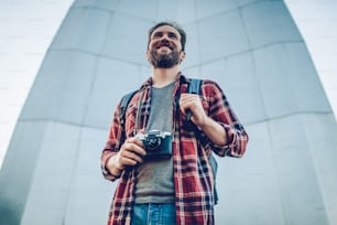 Handsome man is exploring new city. Male tourist with retro camera in hands in search of adventures.