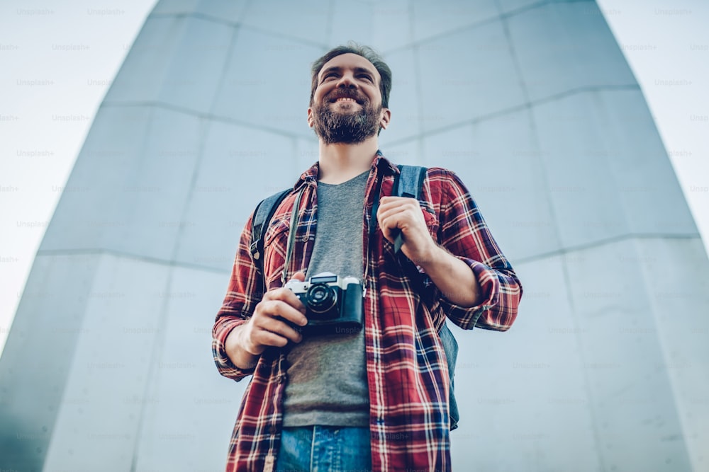Handsome man is exploring new city. Male tourist with retro camera in hands in search of adventures.