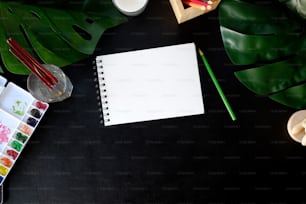Table de bureau en cuir d’artiste avec fournitures créatives, aquarelle et fleur. Vue de dessus avec espace de copie