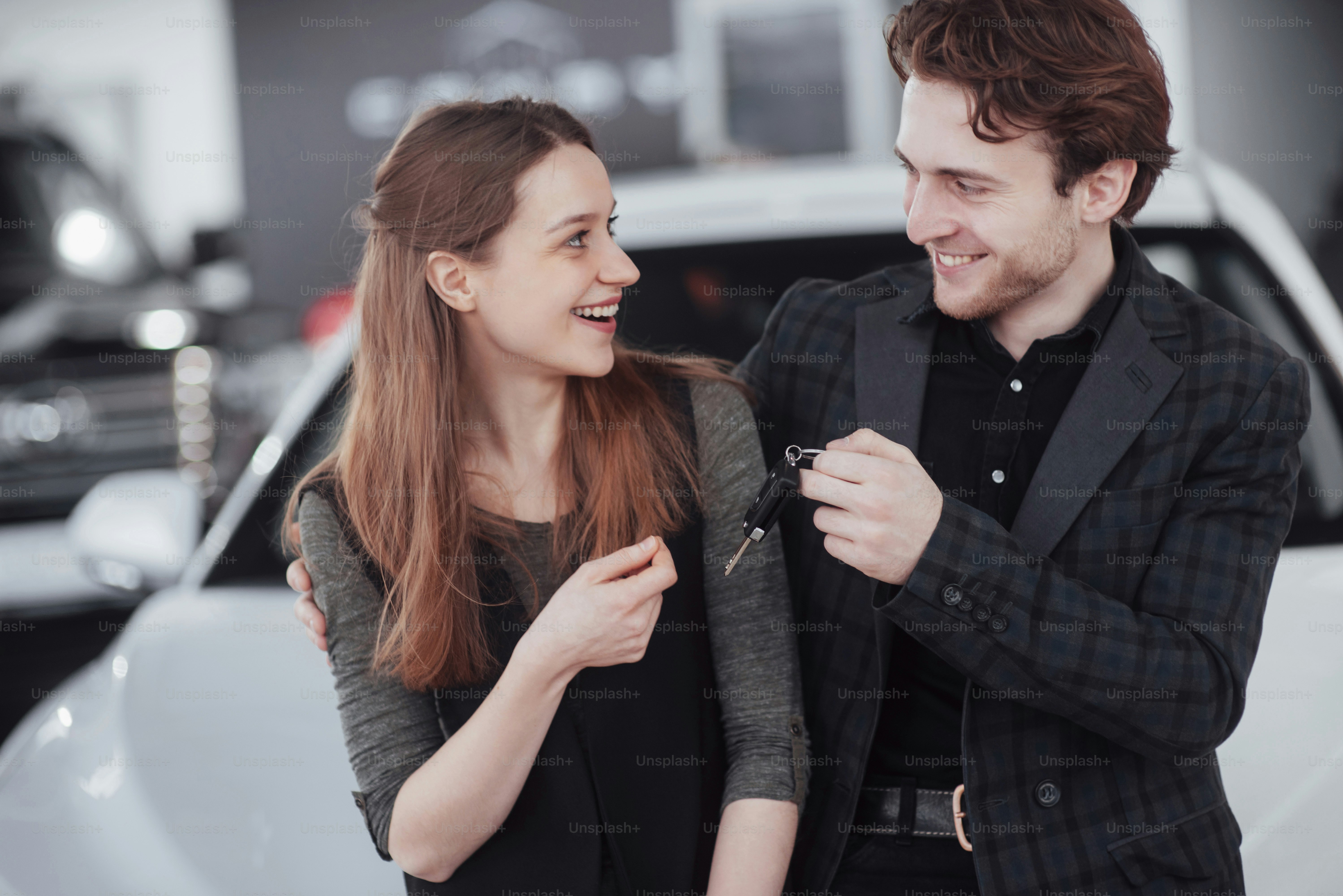 Now her dream comes true. Car salesman giving the key of the new car to the young attractive owners.