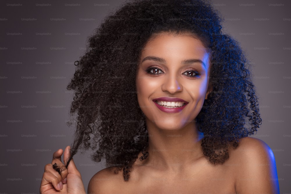 Beauty portrait of smiling dark skin young woman with curly afro hair and glamour makeup. Studio  shot on gray background, copy space.