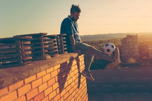 Giocatore di football sul tetto di un edificio, seduto e rilassato dopo la partita, tenendo un pallone