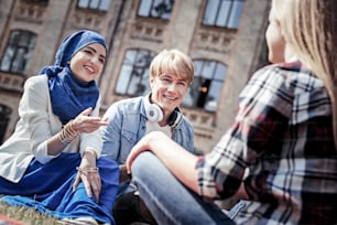 Pleasant interaction. Delighted positive nice students sitting together and having a conversation while being in a wonderful mood