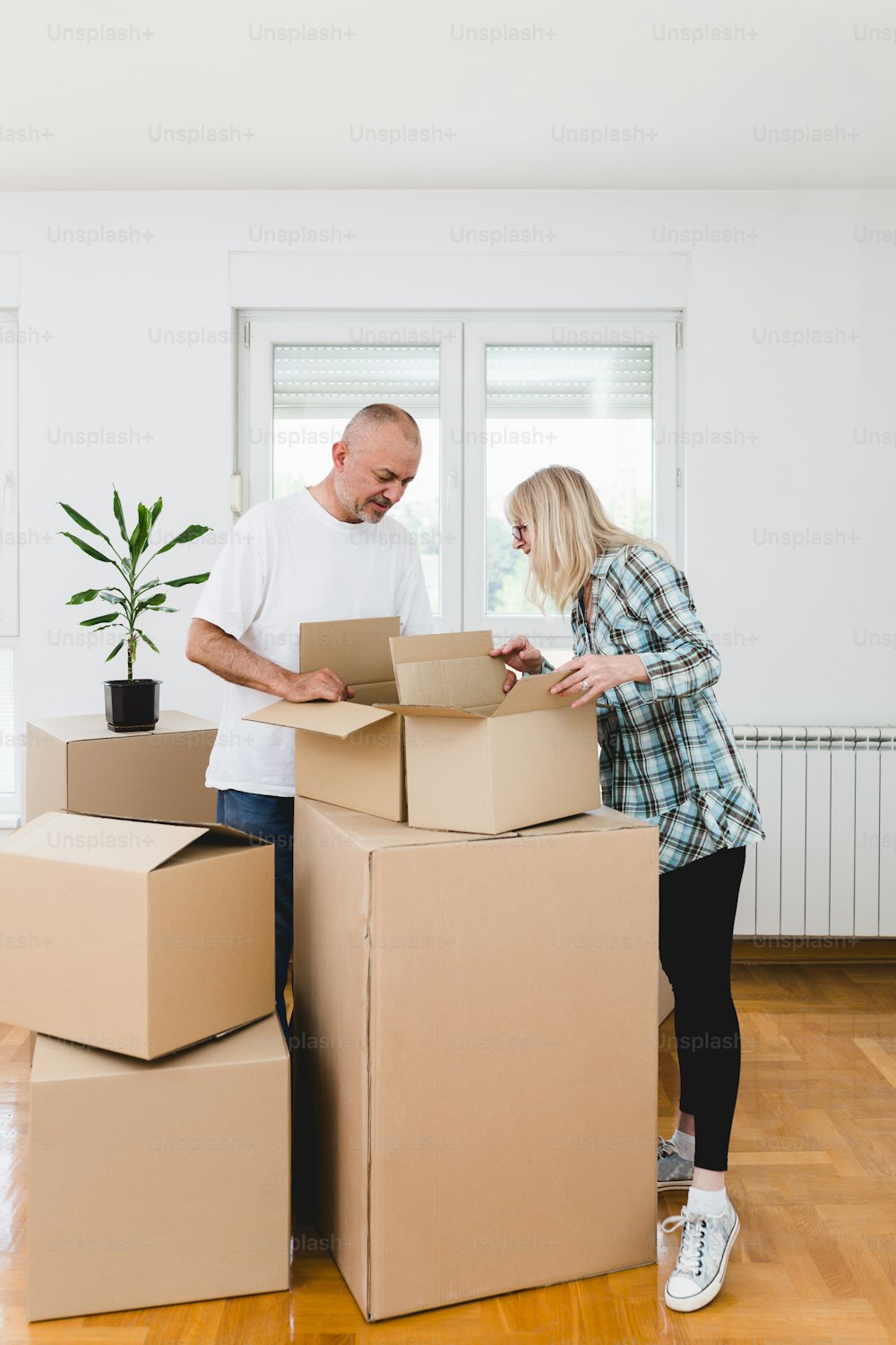 Happy middle age couple moving into new apartment. They standing and holding carton boxes.