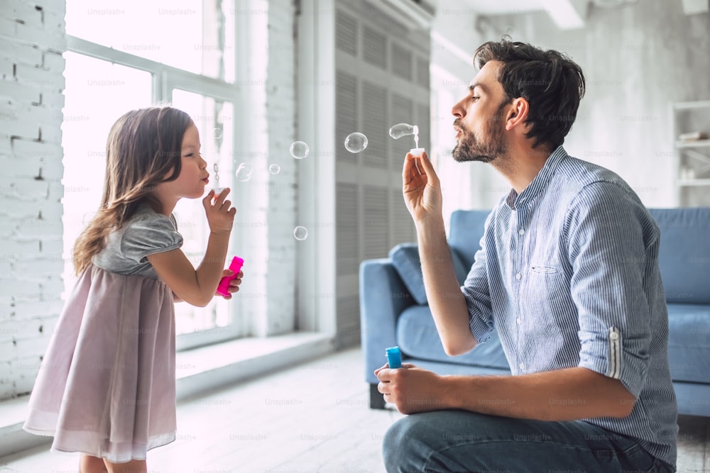 I love you, dad! Handsome young man at home with his little cute girl are having fun and blowing soap bubbles. Happy Father's Day!