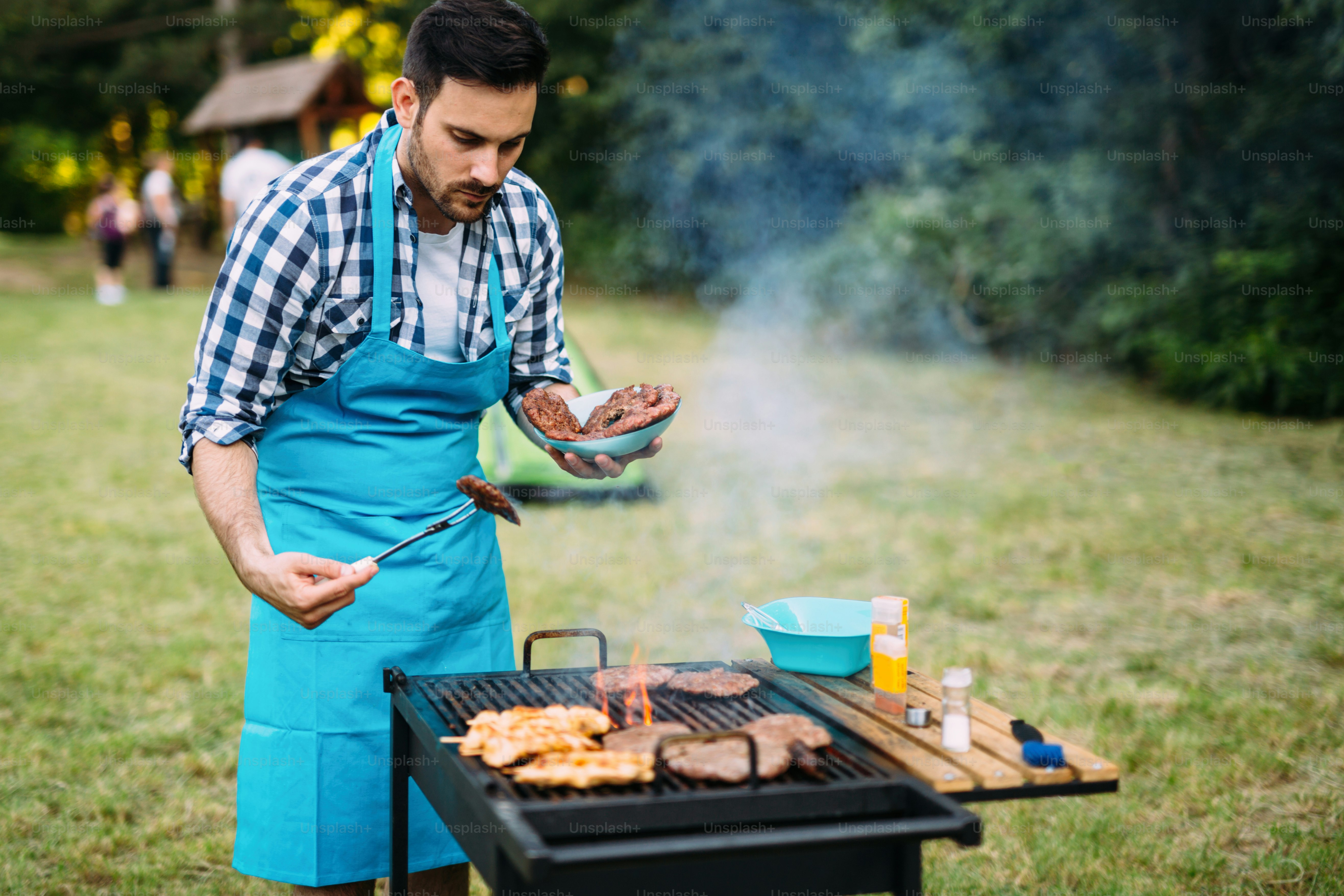 Carne de barbacoa a la parrilla masculina feliz al aire libre en la naturaleza