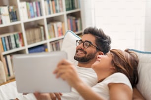 Couple in love, lying in bed, surfing the web on a tablet computer, reading the news