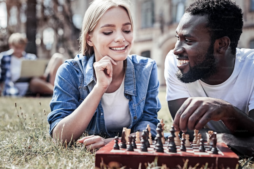 Smart move. Delighted thoughtful nice woman looking at the chess board and smiling while thinking about her next move