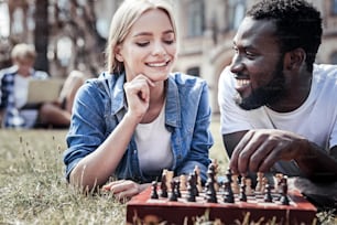 Smart move. Delighted thoughtful nice woman looking at the chess board and smiling while thinking about her next move
