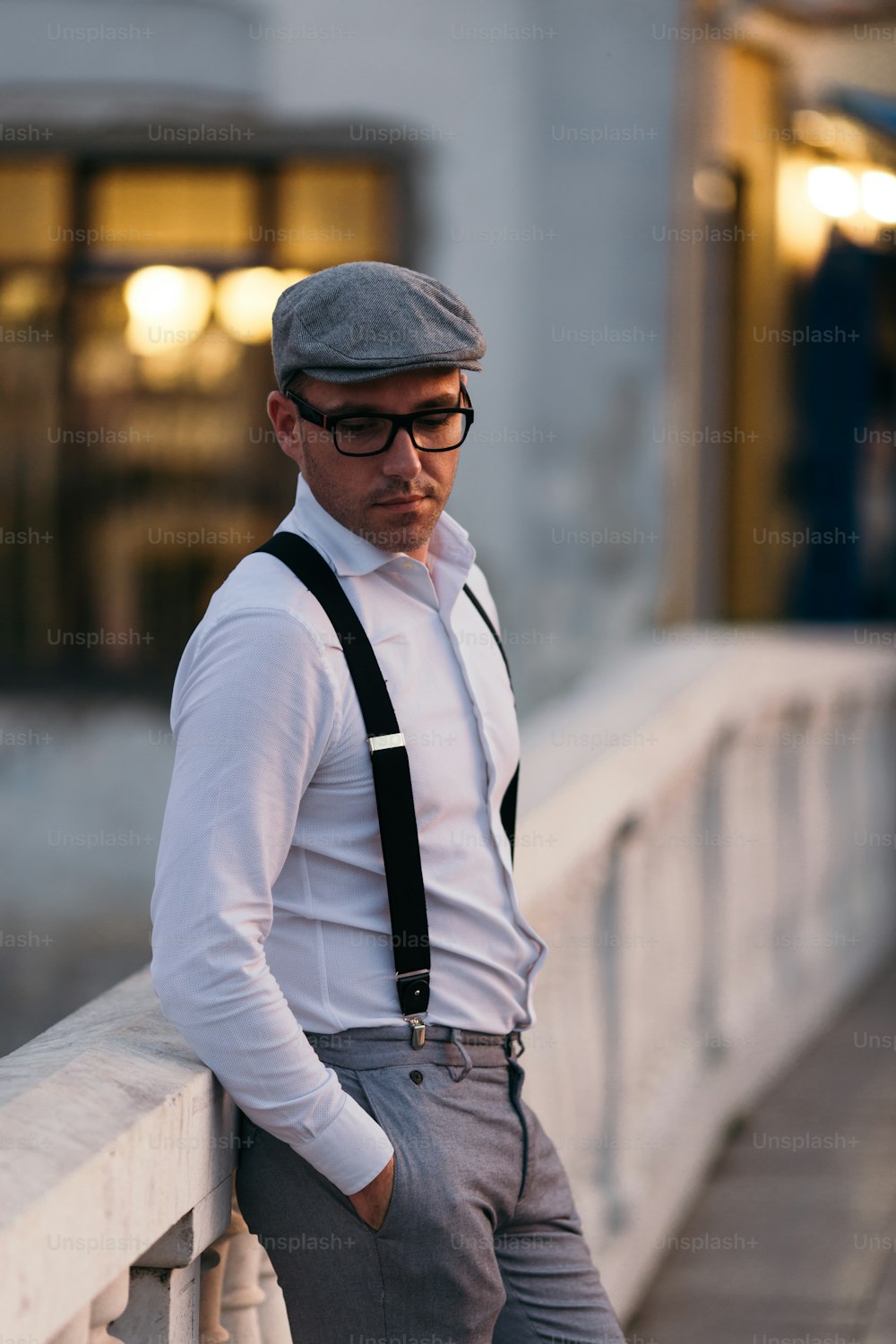 Modischer Retro-gekleideter Mann mit Mütze, Hosenträgern und Brille, der auf der Stadtstraße steht und zur Seite schaut. Niedrige Winkelansicht.