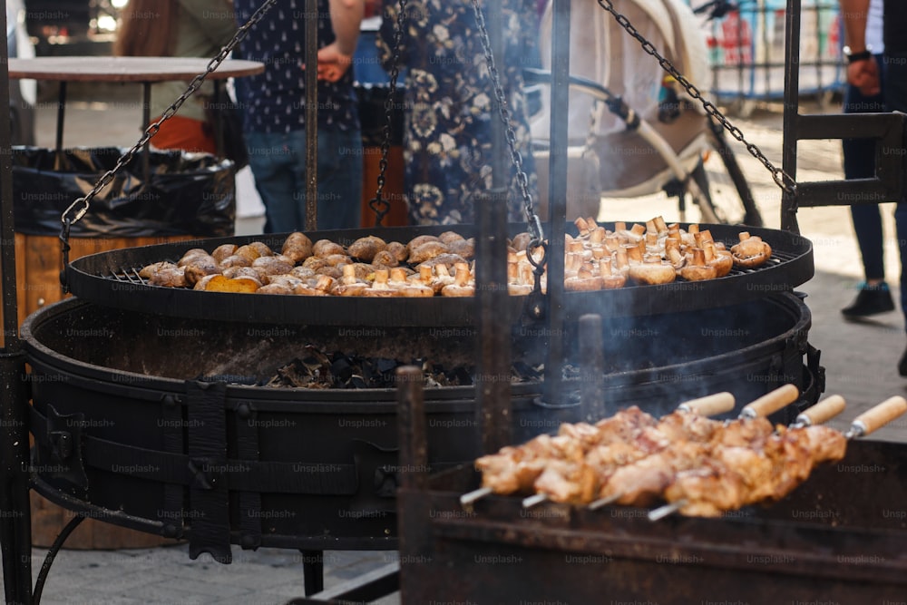 Délicieuses pommes de terre et champignons rôtis au barbecue sur un gril ouvert, cuisine extérieure. Festival de la nourriture dans la ville. Savoureux légumes grillés et viandes, aire de restauration. pique-d’été.