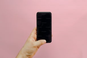Hand hält stilvolles schwarzes Telefon mit leerem Bildschirm auf rosa Hintergrund, flach gelegt. Platz für Text. Modernes Instagram-Bloggen. Sommerferien. Social Media und Kommunikation