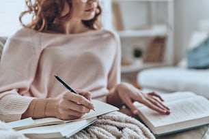 Nahaufnahme von jungen Frauen, die etwas aufschreiben, während sie zu Hause auf dem Sofa sitzen