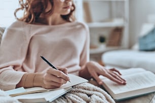 Close up of young women writing something down while sitting on the sofa at home