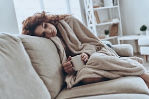 Giovani donne malate coperte da una coperta che riposano a casa mentre sono sedute sul divano