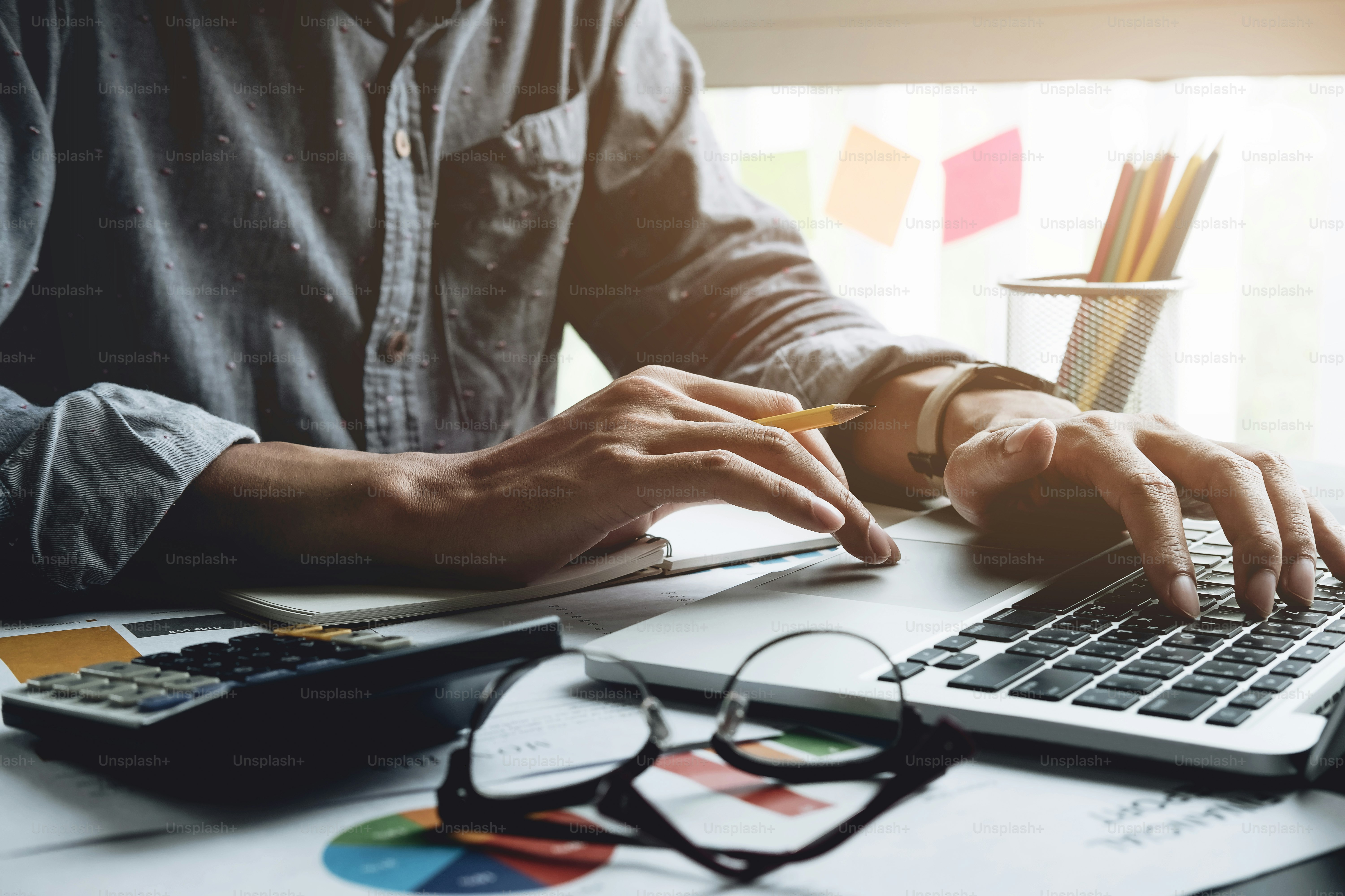 Close up of businessman or accountant hand holding pen working on calculator to calculate business data, accountancy document and laptop computer at office, business concept
