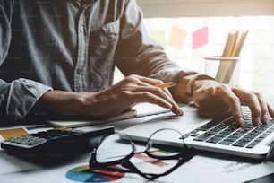 Close up of businessman or accountant hand holding pen working on calculator to calculate business data, accountancy document and laptop computer at office, business concept