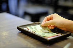 Primer plano sosteniendo la mano de Bill con billete de banco de dinero tailandés y monedas (propina) en el cambio de recibo de efectivo del restaurante