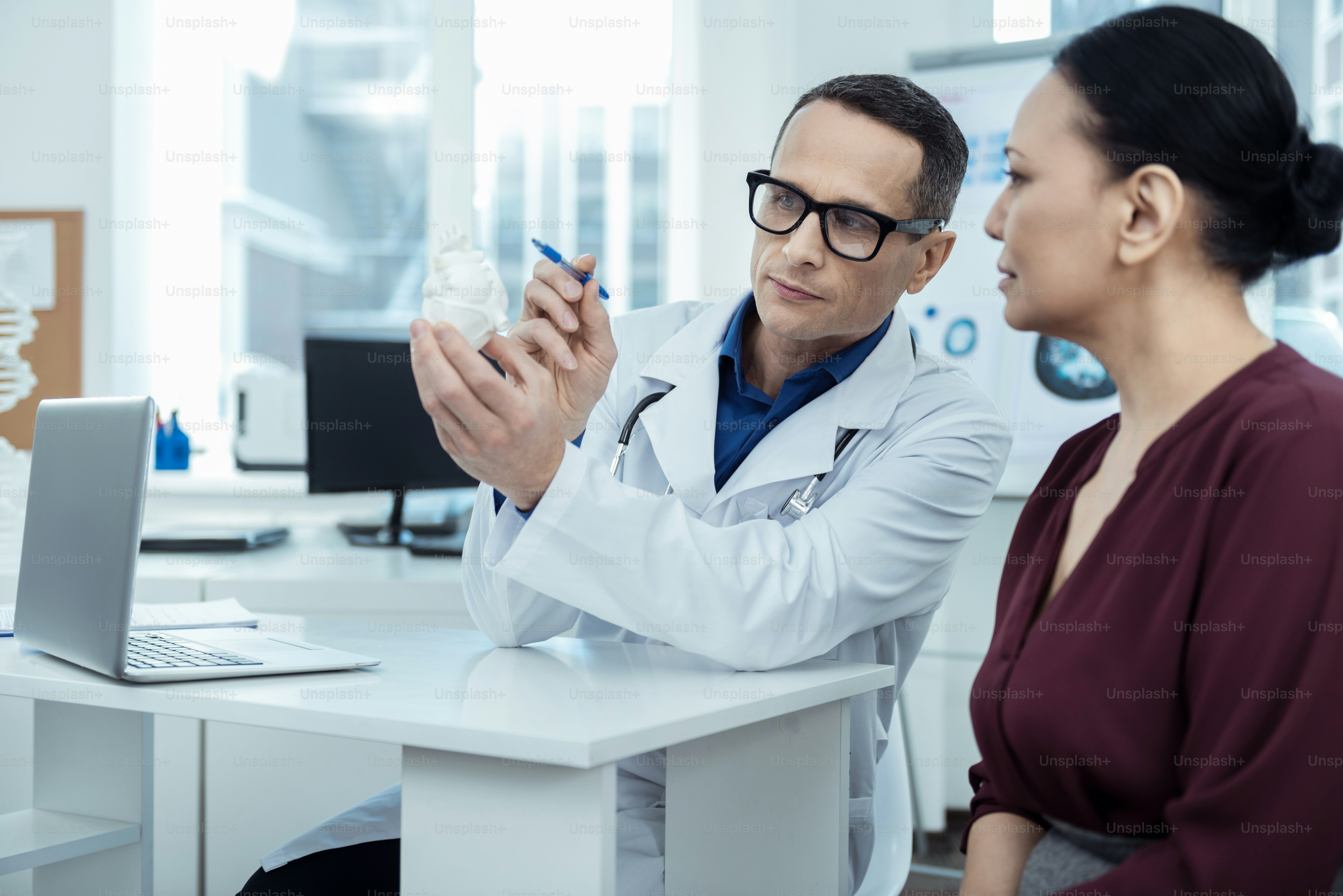 This vessel. Professiononal doctor showing a model of heart to his patient