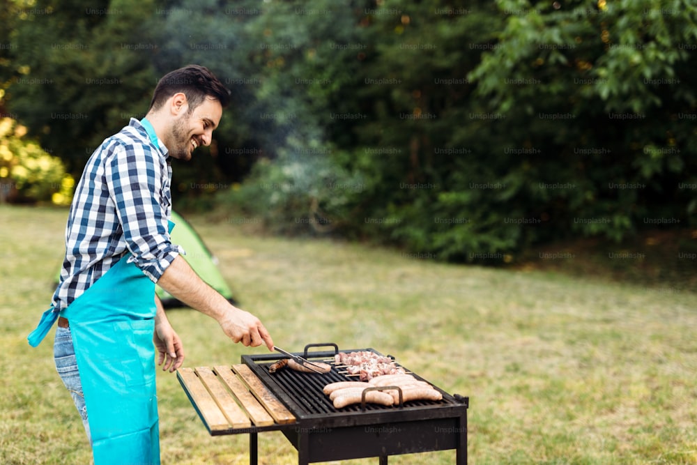 Handsome young male prepares barbecue outdoors in forest