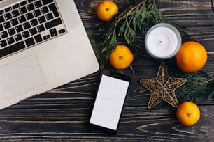 christmas flat lay of laptop and phone with empty screen and branches and oranges and star on black rustic wooden desk. space for text. seasonal shopping online concept
