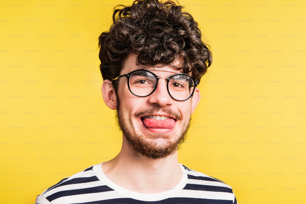 Studio portrait of a young handsome man sticking out his tongue on a yellow background. Close up.