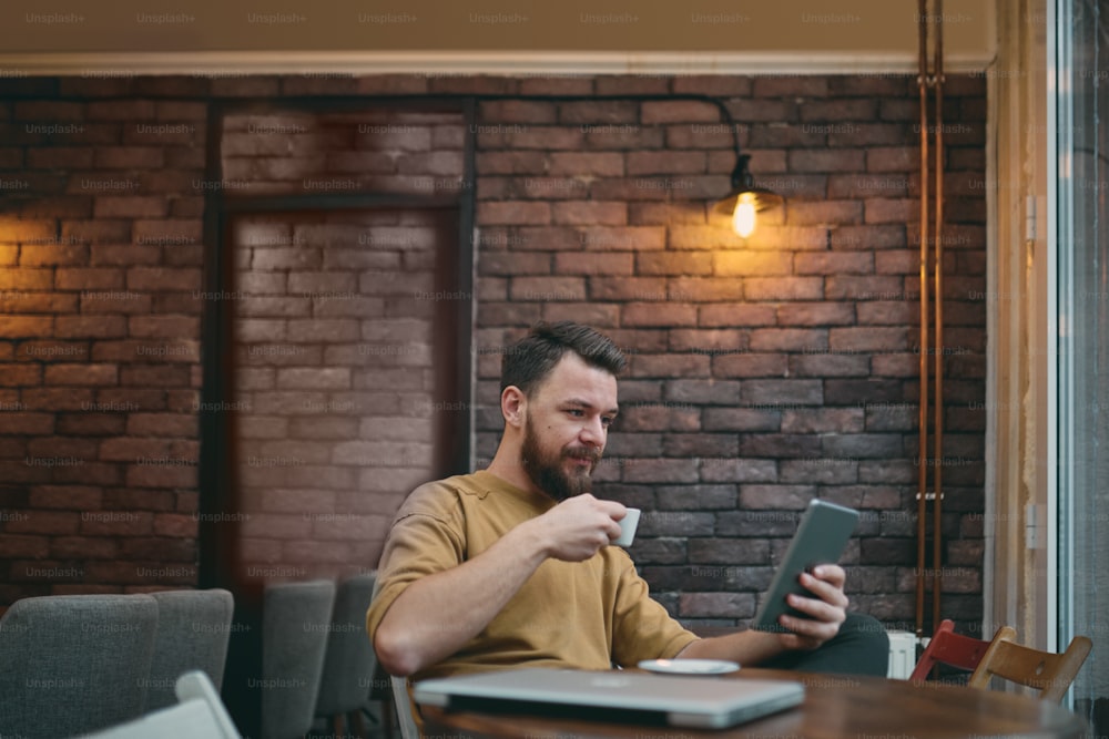 Mann benutzt Laptop und Smartphone, während er im Café sitzt. Konzept der neuen Technologien