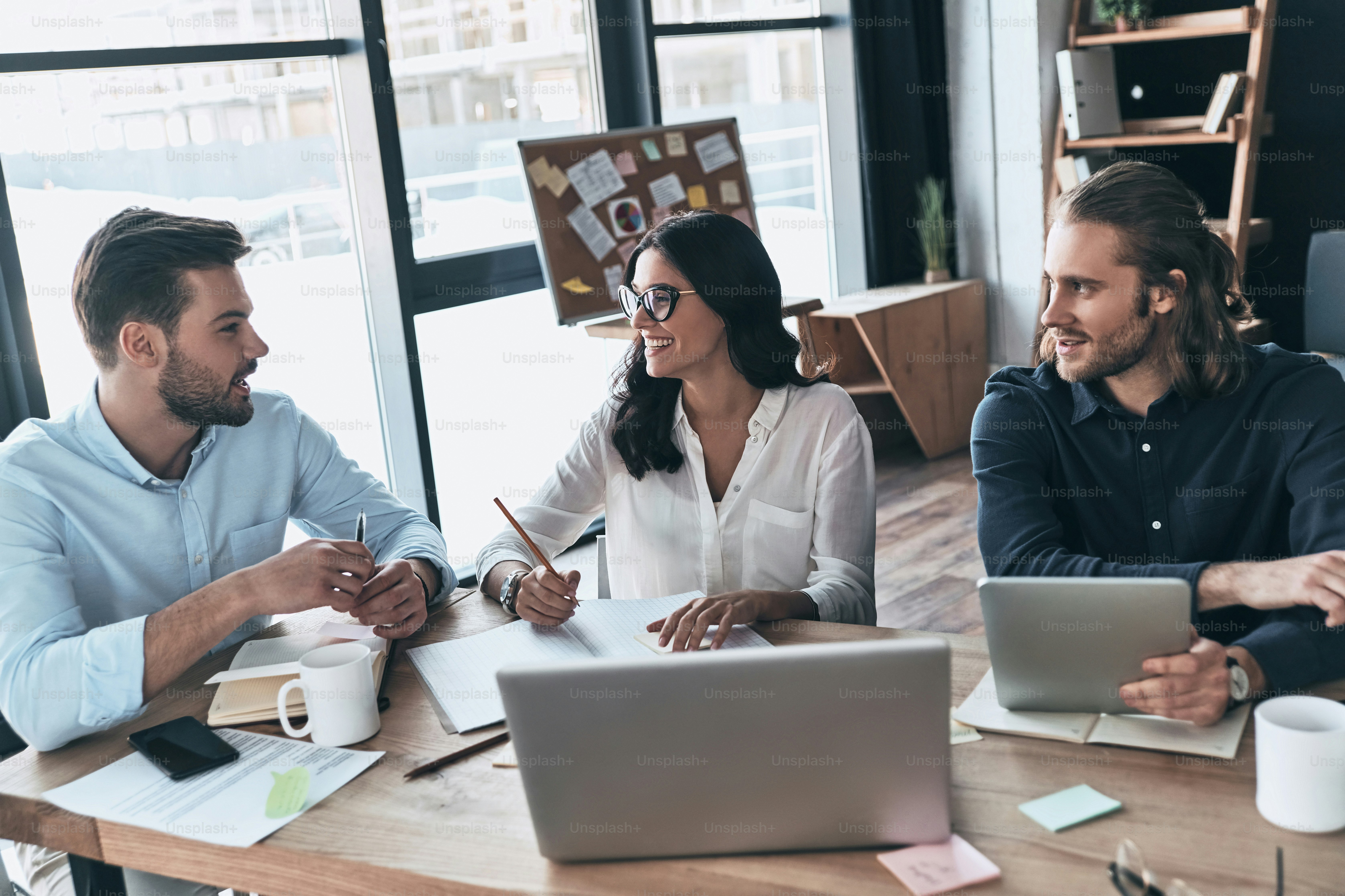 Group of young modern people in smart casual wear working together and smiling while sitting in the creative office