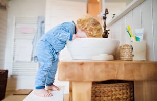 Cute toddler in the bathroom. Little boy putting a head in a sink. Domestic accident. Dangerous situation.