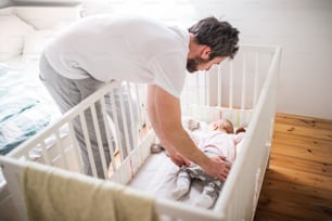 Mature father putting a sleeping toddler girl into a cot at home. Paternity leave.