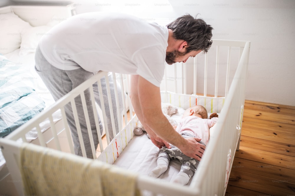 Reifer Vater, der ein schlafendes Kleinkind zu Hause in ein Kinderbett legt. Vaterschaftsurlaub.