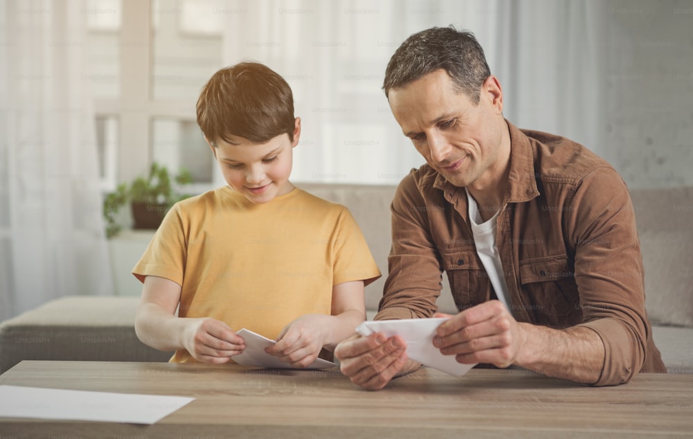 Cheerful family folding papers into decorative shapes. They are sitting at desk and smiling