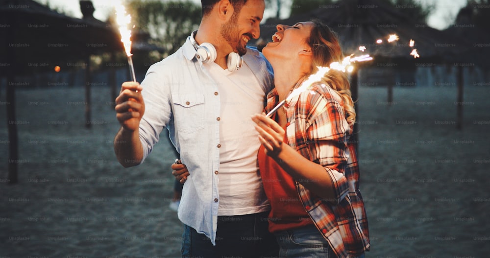 Group of happy friends having fun on beach at night playing with sparklers