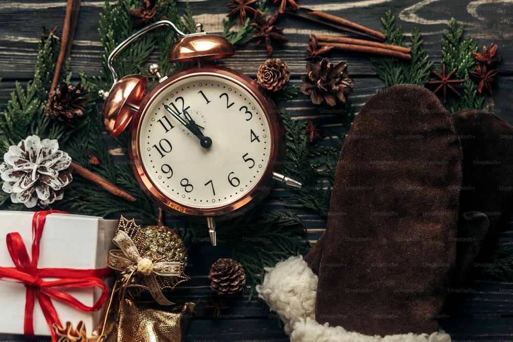 new year midnight concept. stylish vintage clock with almost twelve hour and presents ornaments and branches on christmas rustic wooden background flat lay. 2017 winter holidays