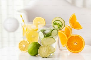 Glasses of infused water with fresh lime, cucumber and mint leaves, lemon and orange. Selective focus on the lime half