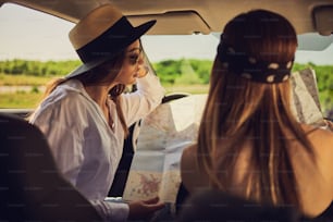 Due ragazze sedute in macchina e che leggono la mappa.