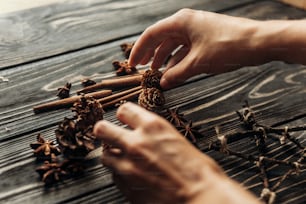 stylish rustic winter picture with hands arranging anise and pine cones on wooden background. space for text. cozy mood autumn. seasonal holidays concept