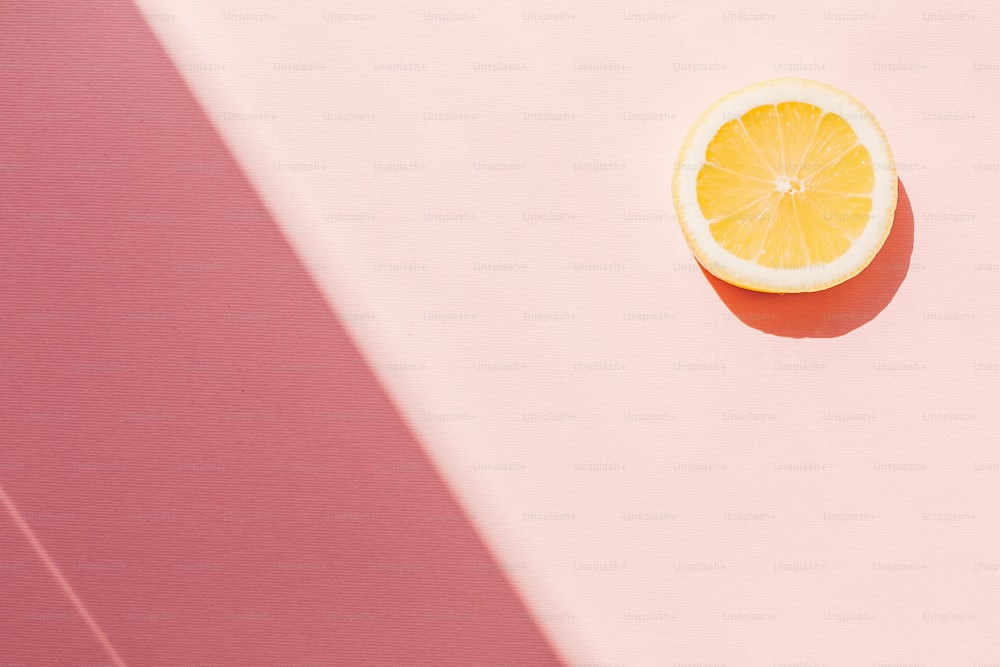 Scheibe gelbe Zitrone auf trendigem rosa Papierhintergrund flach gelegt, in hellem Sonnenlicht. Sommerobstkonzept, buntes Muster. Urlaubsstimmung. Cocktail- und Getränkekonzept. Platz für Text