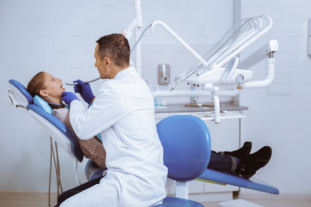 Oral hygiene. Serious dentist sitting in semi position while examining his patient