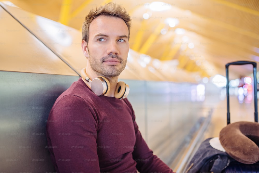 Young man waiting listening music and using mobile phone at the airport with a suitcase