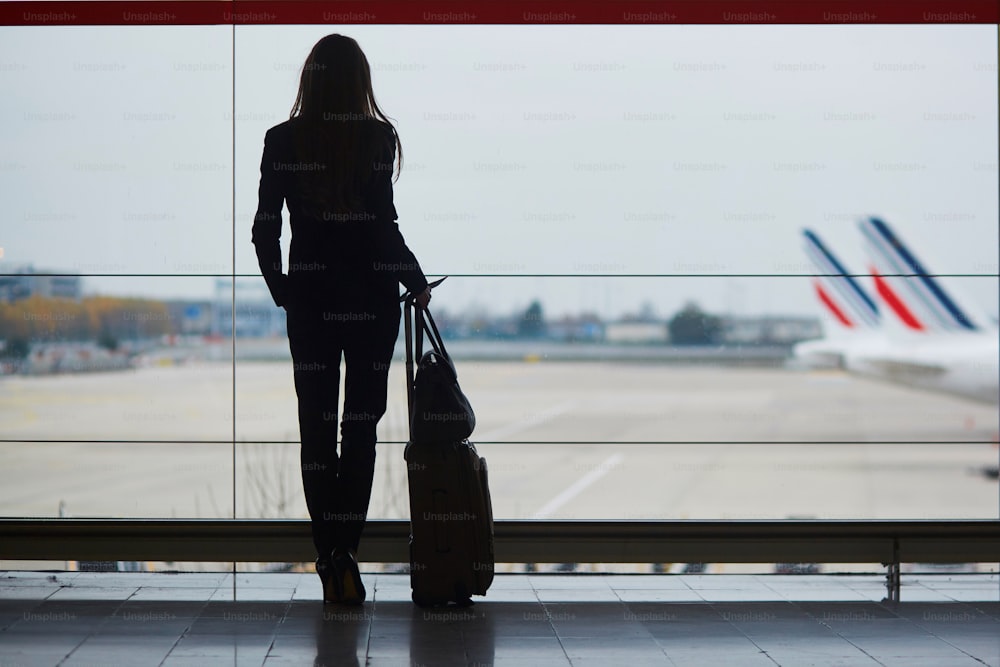 Mulher nova no aeroporto internacional olhando para os aviões através da janela
