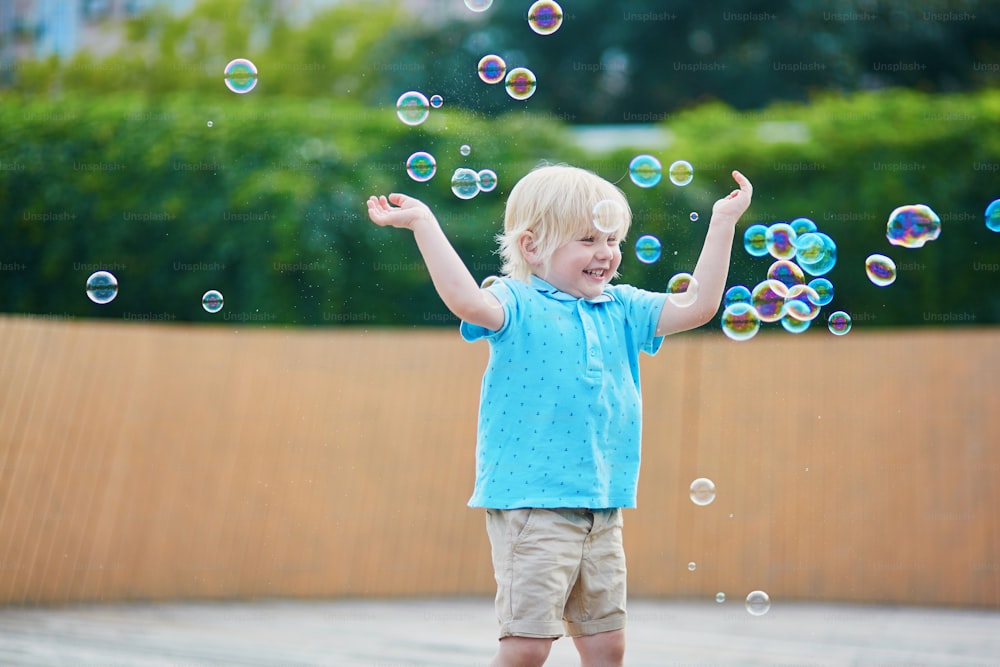 Menino feliz adorável brincando com bolhas ao ar livre em um dia de verão