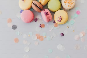 Délicieux macarons colorés sur papier gris pastel tendance avec des fleurs lilas et des confettis, pose à plat. Savoureux macarons roses, jaunes, verts et bruns. espace pour le texte. bonbons pour la fête
