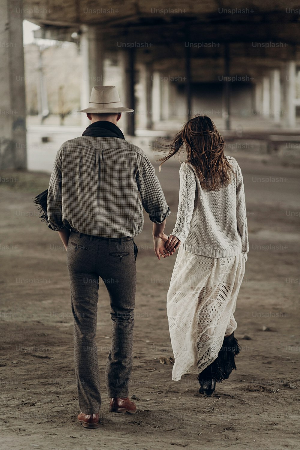 흰 모자를 쓴 잘생긴 텍사스 카우보이 남자가 하얀 드레스를 입은 아름다운 집시 여자와 손을 잡고 있다, 도시에서 산책하는 커플