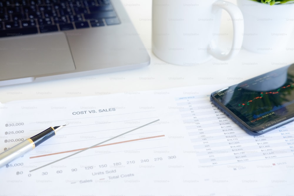 Concetto finanziario di costo, grafico di carta dell'attrezzatura aziendale, penna con computer portatile e smartphone sul tavolo dell'ufficio.