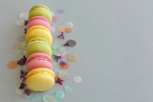 colorful macarons on trendy pastel gray paper with lilac flowers and confetti. tasty pink, yellow, green and brown macaroons. candy bar for party. food photography. yummy background