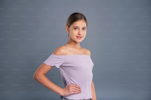 Wannabe model. Charming teenage girl in a lilac strapless top standing half-turned and holding a hand on her waist while smiling at the camera