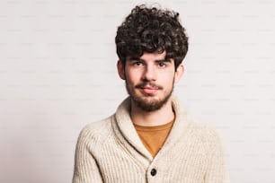 A young handsome man in beige woollen cardigan in a studio. Copy space.