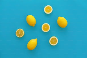 밝은 파란색 종이에 노란색 레몬과 레몬 조각, 트렌디 한 플랫 레이. 과일 현대 이미지, 상위 뷰입니다. 육즙이 많은 여름 비타민과 다이어트 개념. 팝 아트 스타일. 창조적 인 미니멀리즘 패턴